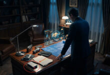 Homme en costume face à un écran holographique interactif sur un bureau d'étude, avec indices et boîtier rouge lumineux.