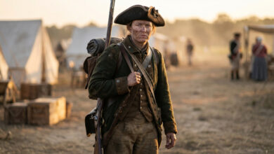Femme soldat historique en uniforme colonial, portant mousquet et équipement, dans un campement militaire au coucher du soleil.