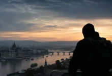 Silhouette d'un homme en bonnet et sac à dos observant le panorama de Budapest au lever du soleil depuis les hauteurs.